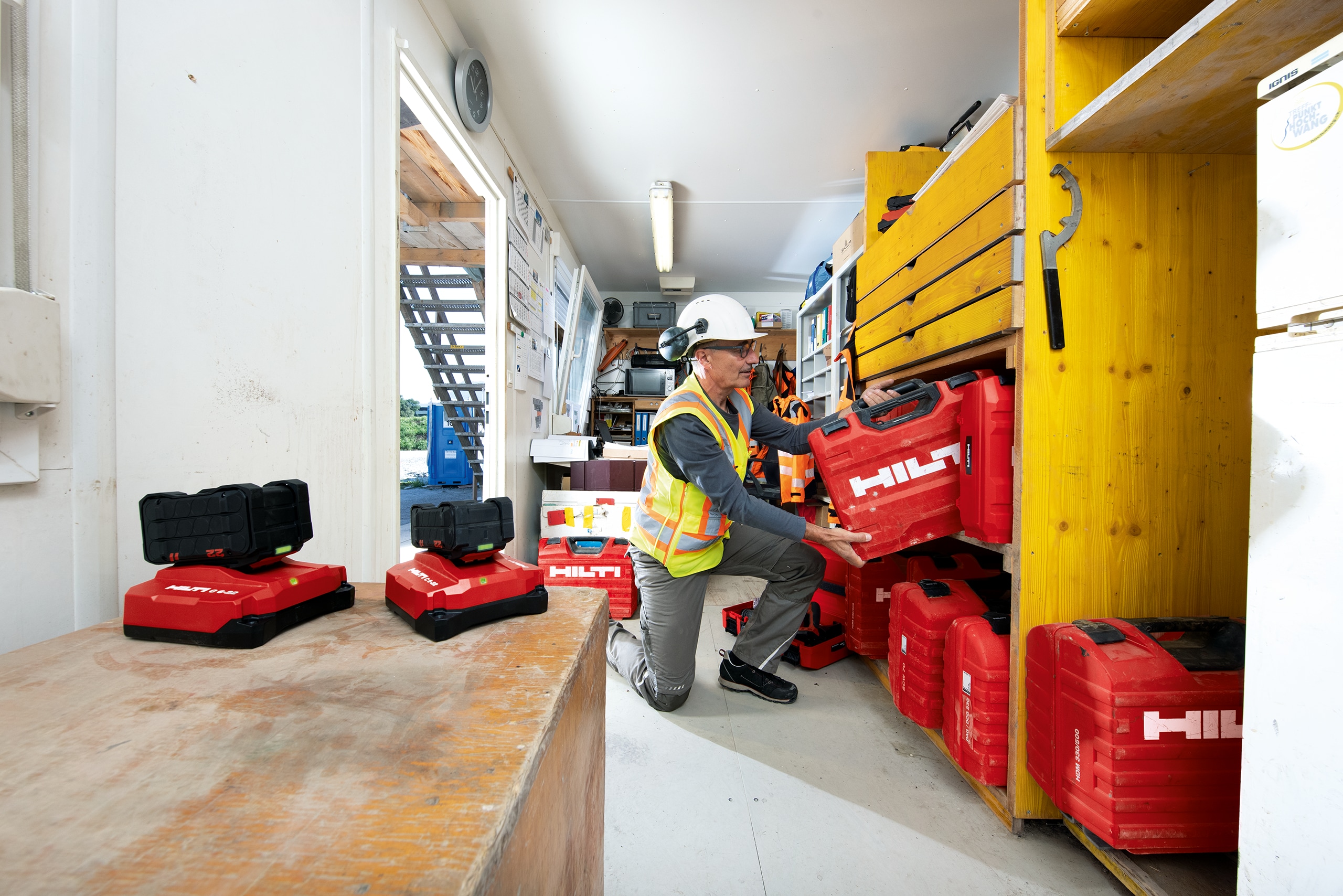 Gestor de conjunto de ferramentas a colocar uma caixa de ferramentas Hilti numa prateleira num contentor de construção